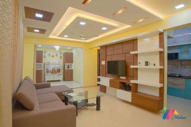 A living room with a wall-mounted television, display shelving and a recessed ceiling.