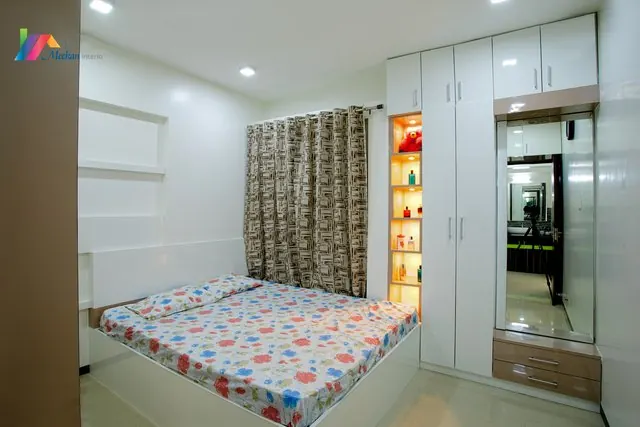 A bedroom with white fitted cabinets, a mirrored wardrobe and a bedside display niche.