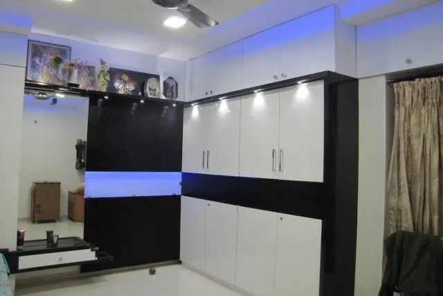 A bedroom wardrobe in white and dark finishes with blue ceiling lighting.