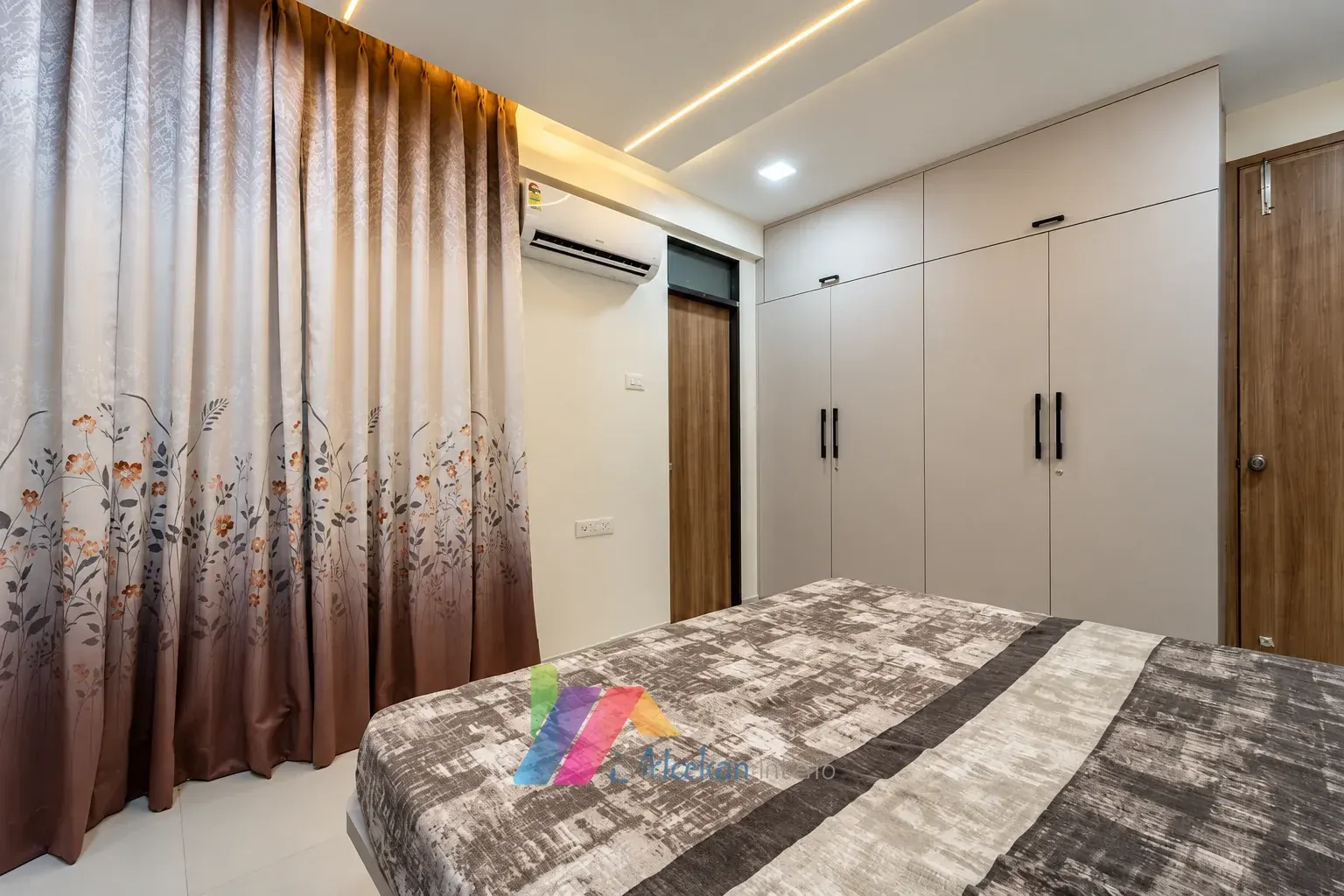 Bedroom with fitted white wardrobes, patterned curtains and a broad bed.