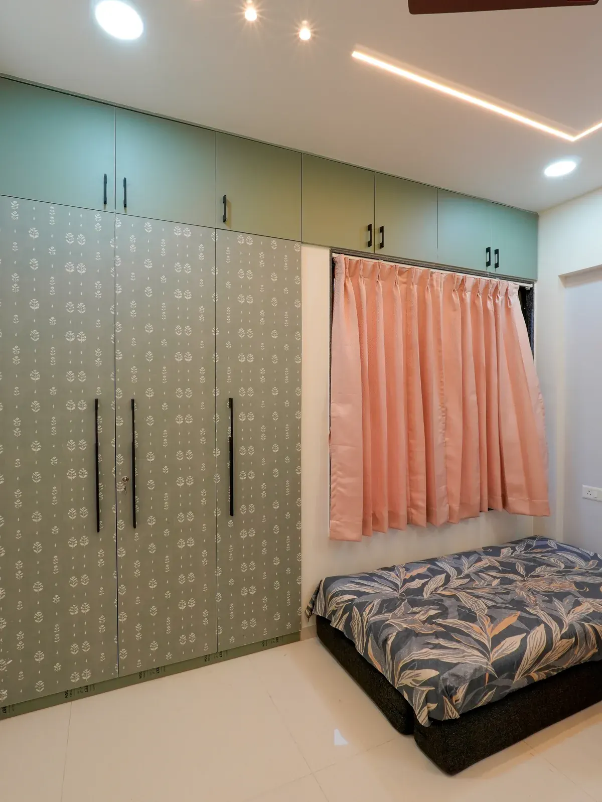 A bedroom with patterned wardrobe doors, mint overhead cupboards and peach curtains.