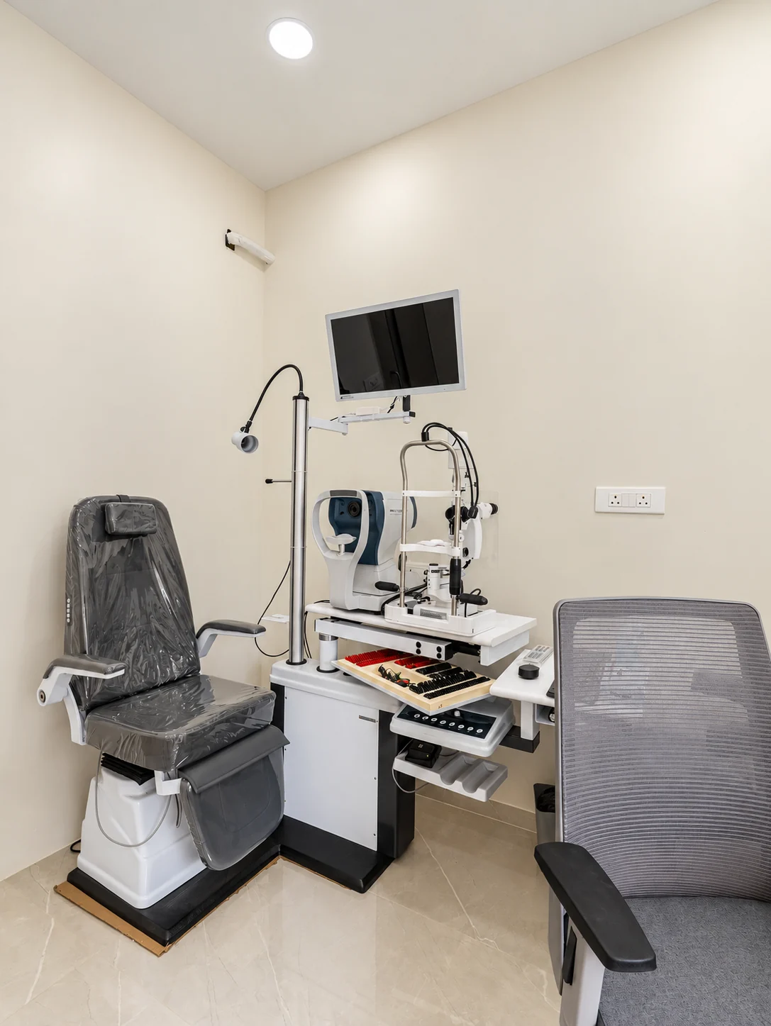 Eye examination room with a patient chair, diagnostic equipment and wall-mounted screen.