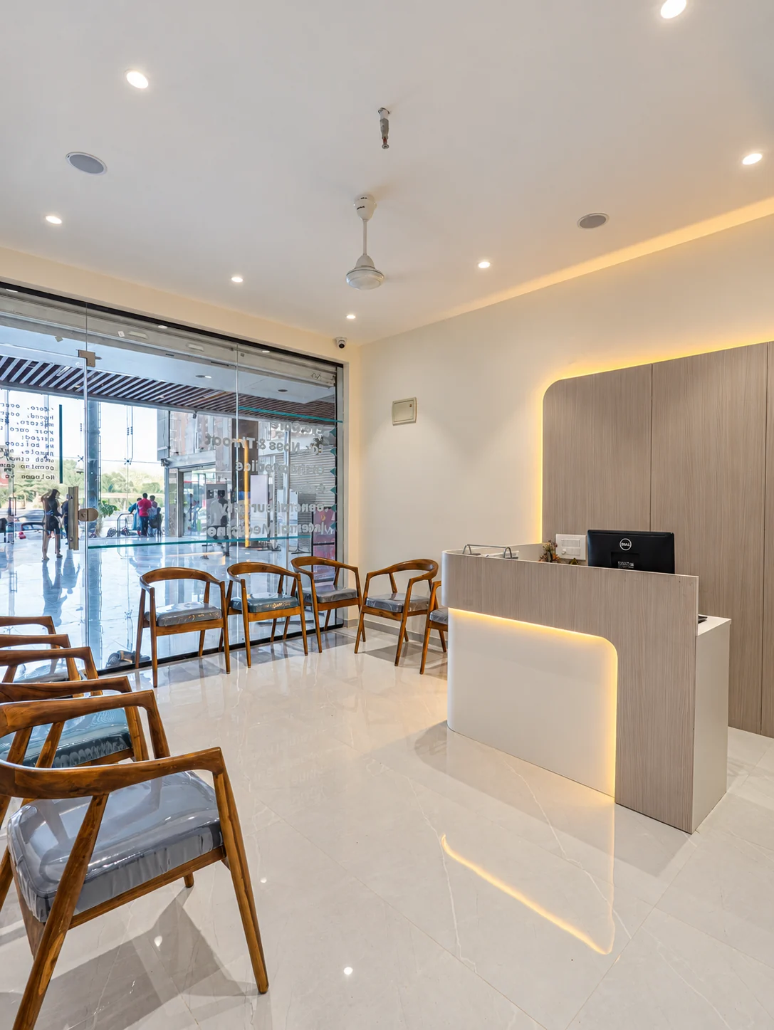 Clinic waiting area with timber chairs beside the glass entrance and a softly lit reception desk.